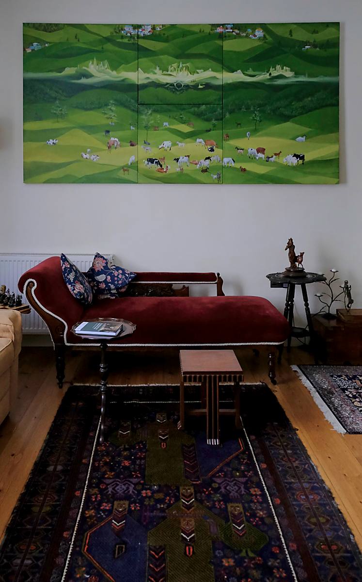 The sitting room, with a green landscape painting above a red sofa
