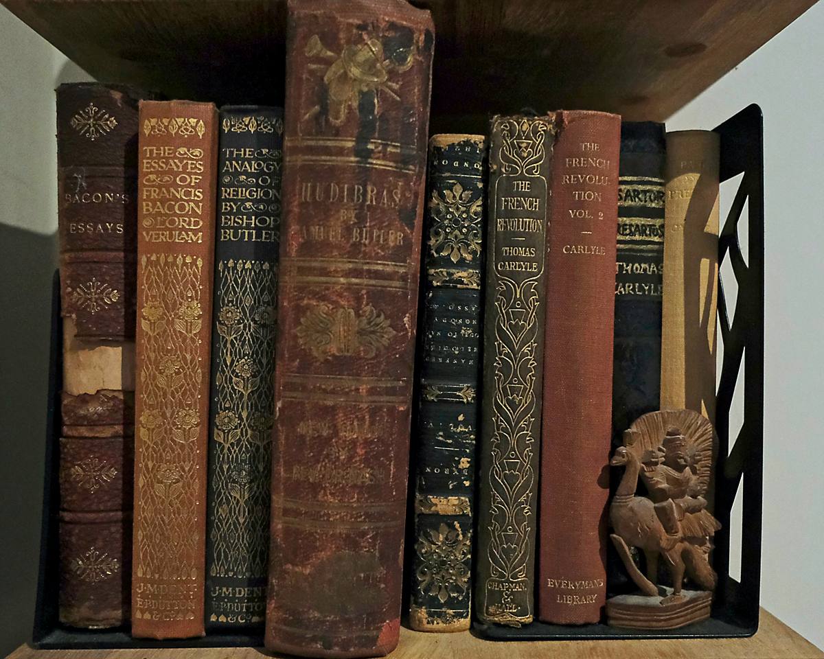 A shelf of old leather-bound books beside a carved wooden figure