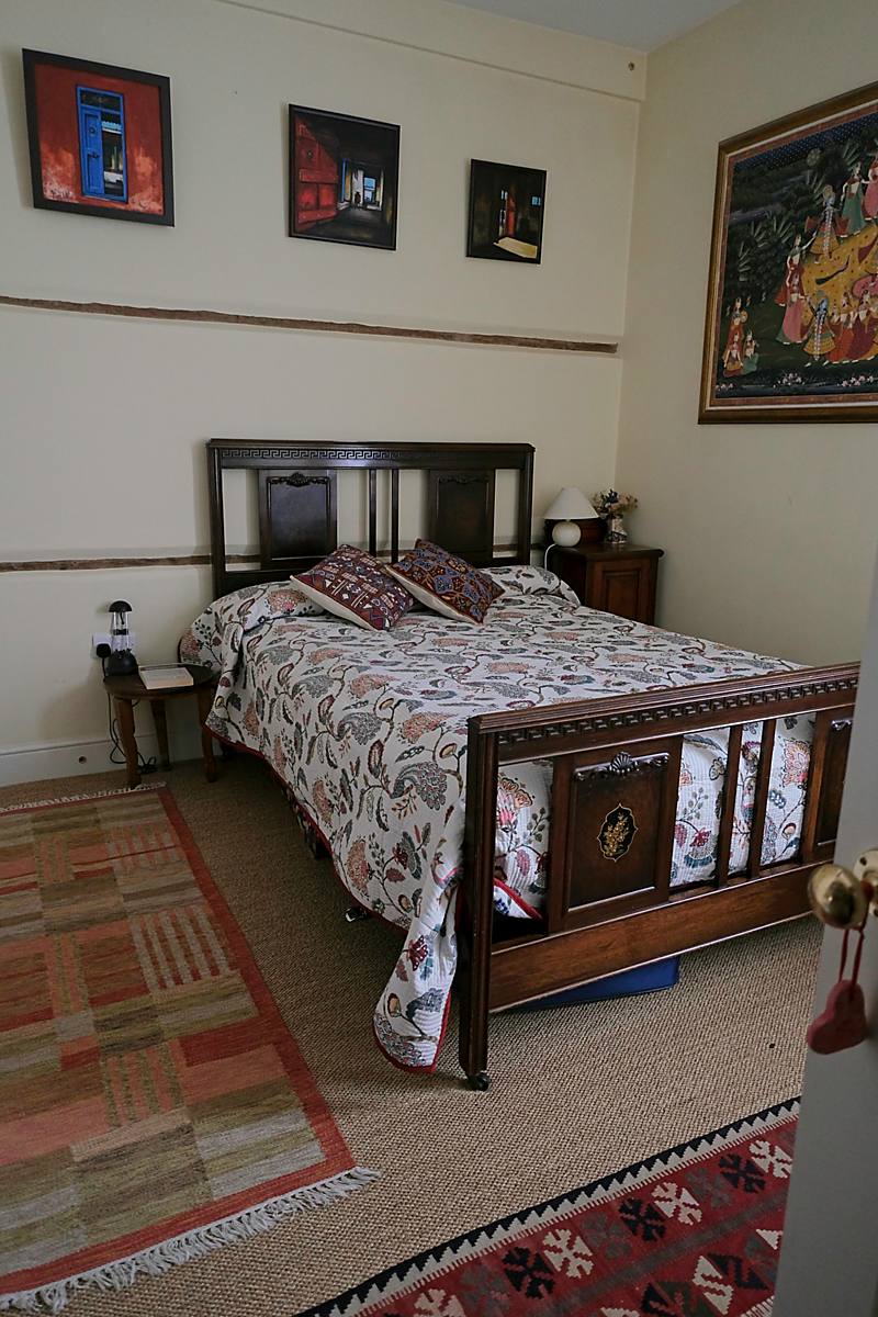 A bedroom with a carved wooden bed and rugs on the floor